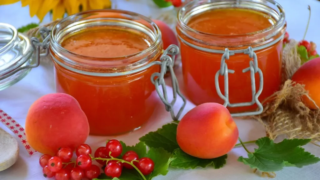 Deux pots de confiture d'abricots entourés d'abricots frais et de groseilles