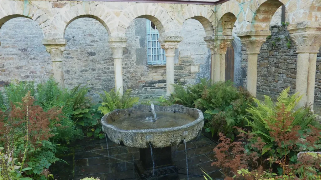 Une vasque de pierre au milieu des plantes dans le cloître de l'abbaye de Daoulas
