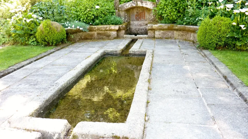 Un long bassin de granit et sa fontaine adossée à un jardin, en Finistère