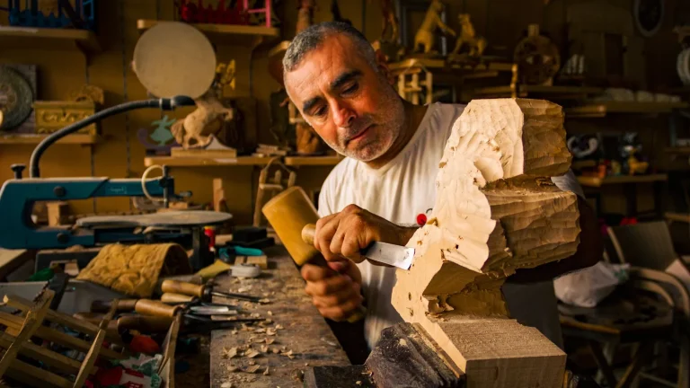 Un artisan sculpte une pièce de bois à la gouge et au maillet dans son atelier