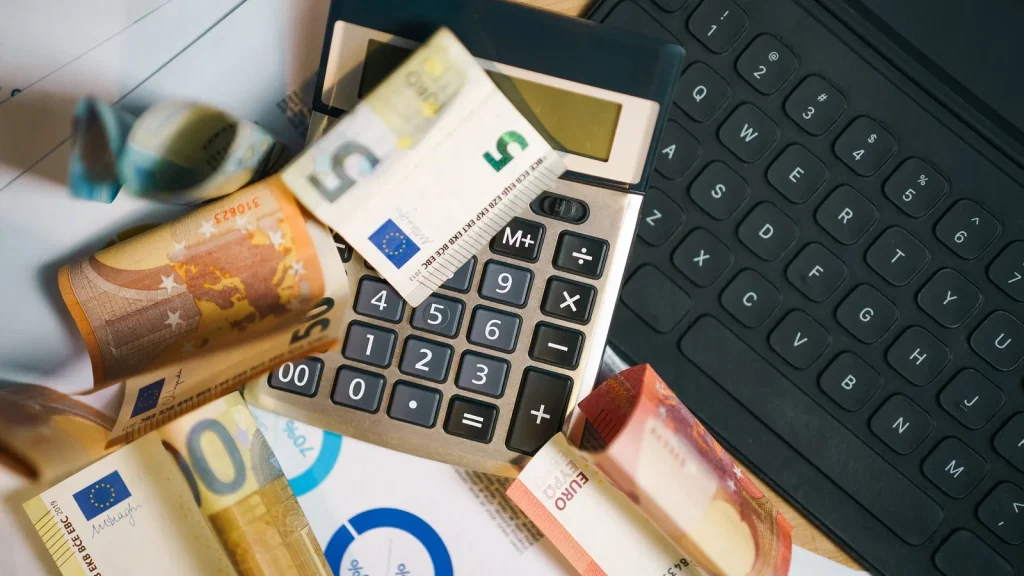 Des billets en euros et une calculatrice posés près d'un clavier d'ordinateur