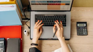 Une personne remplit sa déclaration sur un ordinateur portable, avec une calculatrice sur le bureau