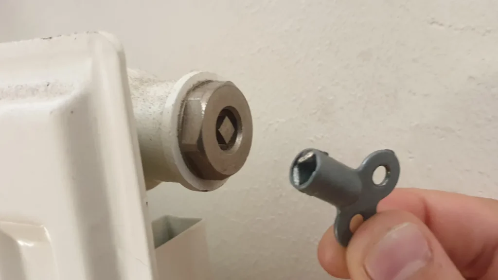 Une main présente la clé de purge devant la vis d'un radiateur blanc
