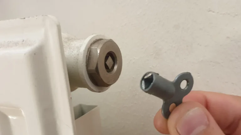 Une main présente la clé de purge devant la vis d'un radiateur blanc