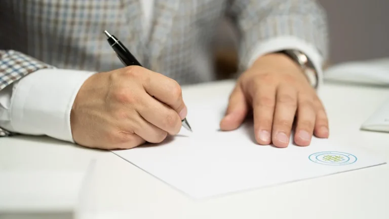 Un homme en veste signe un contrat de prêt sur un bureau blanc, stylo à la main