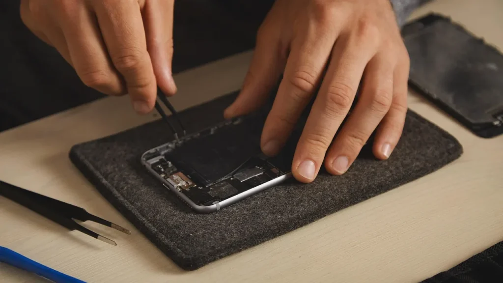 Mains d'un réparateur qui ouvre un smartphone en panne sur un tapis d'atelier