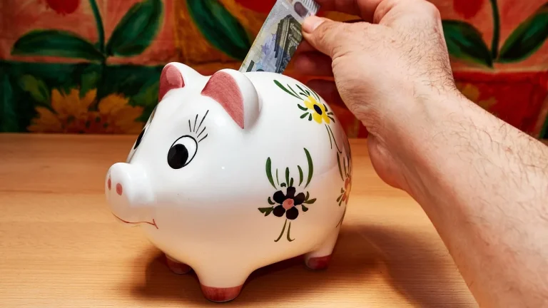Une main glisse un billet en euros dans une tirelire en céramique
